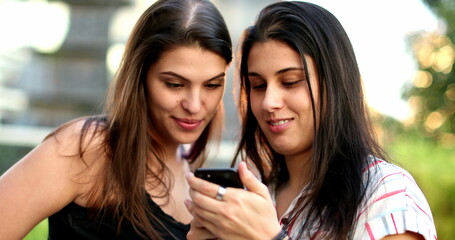 Women using smartphone outside. Female friends checking cellphone screen