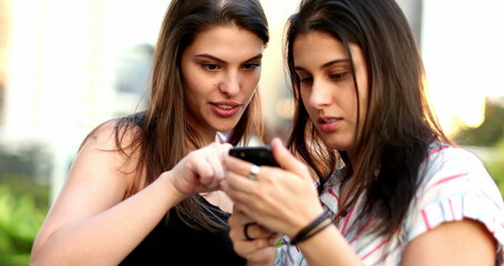 Women using smartphone outside. Female friends checking cellphone screen