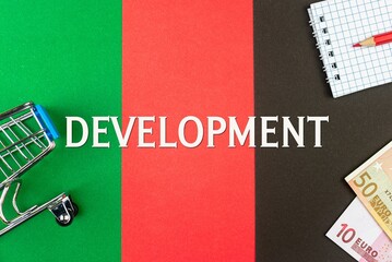 DEVELOPMENT - word (text) and euro money on a table of different colors, a trolley, a basket of grocery notepad and a red pencil. Business concept, buying, selling, supermarket, store (copy space).