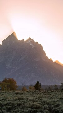 Time lapse of sun rays beaming from behind the Grand Teton Mountains during sunset.