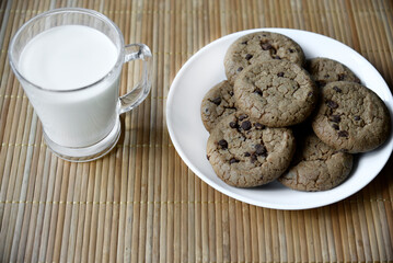 A glass glass with milk on a wooden mat with oatmeal cookies. Afternoon lunch with cookies. Sweet cookies with milk.