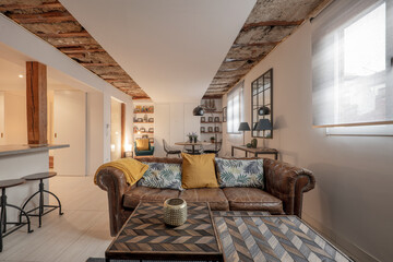 Living room with many wooden furniture and leather sofas with cushions and industrial style stools