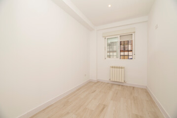 Empty room with light wood floorboards, white painted walls and barred window