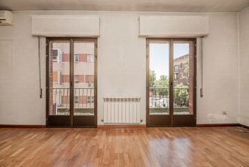 Obraz premium Empty living room with oak wood floor, white painted walls, and two windows leading to an elongated balcony with views