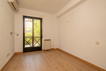 Empty living room with oak wood floor, white painted walls and window with black metal balcony overlooking the garden