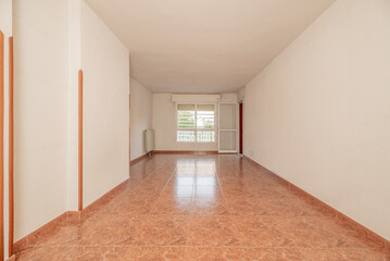 Empty room with a reddish stoneware floor, white painted walls and red carpentry, a large window in the background and a metal and glass door leading to a terrace