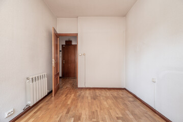 Empty room with oak wood floor, white painted walls and matching woodwork, aluminum radiator and sockets