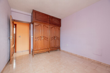 Empty room with pink stoneware floor, light purple painted walls and matching woodwork and wooden cabinets with abandoned chests