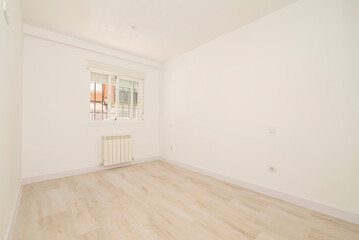 Empty room with very light wooden flooring, off-white painted walls and matching carpentry, aluminum radiator, matching window and flood of light