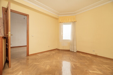 Empty room with shiny oak hardwood floor, matching woodwork, cream walls and curtained window