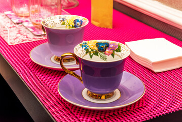 Decorated cups of violet tea service on a pink mat