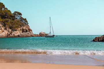Coastal landscape with rocky hills and trees. Boat or yacht sailing on the shore on Costa Brava in Spain