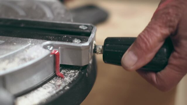 close-up view worker changes the angle rotation of the miter saw. large black handle and red rail.