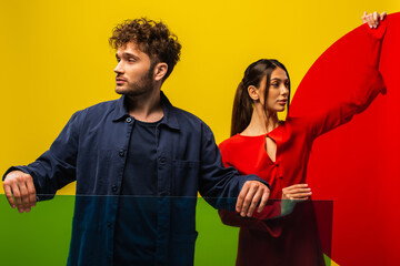 trendy man and woman holding different shapes glass while posing isolated on yellow.