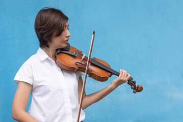 Beautiful woman hold violin on blue wall background, in emotion feeling happy.