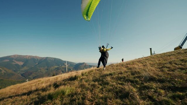 Paraglider taking off in the blue sky with mountain in background.