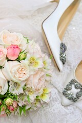 Wedding composition with silk white shoes, pastel bridal bouquet on white lace blurry background. Top view