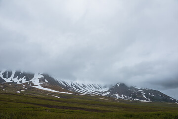 Dramatic alpine landscape with snowy mountains in gray low clouds. Bleak atmospheric scenery of...