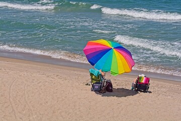 Obraz premium Sunbathers under rainbow colored beach umbrella siting on sandy ocean beach