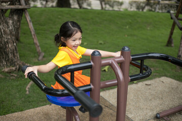 Fototapeta na wymiar Asian happy girl with orange dress is playing in the playground.