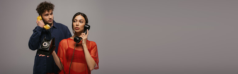 young woman and curly man holding retro handsets while talking isolated on grey, banner.