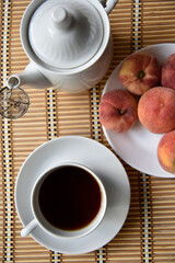 Teapots tea pair with peaches on a plate. Lunch with tea and fruit. Black tea in a white cup.