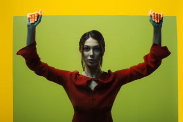 stylish young woman in red dress looking at camera through glass isolated on green.