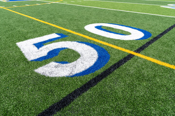 Synthetic turf football 50 yard line in white with royal blue shadow along with black lacrosse line and yellow soccer mid field line 