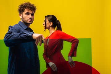 curly man and brunette woman holding different shapes glass while posing isolated on yellow.