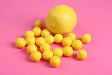 Whole fresh lemon and yellow candies on pink background