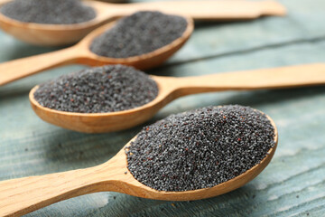 Poppy seeds in spoons on blue wooden table, closeup