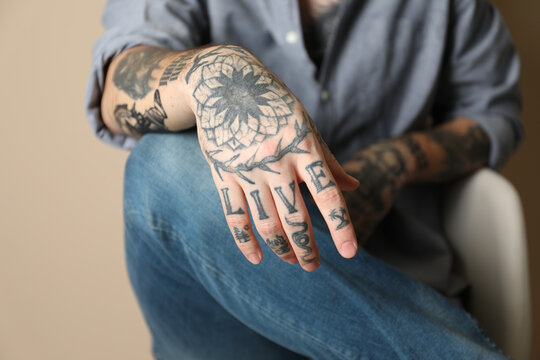 Young man with tattoos on arms against beige background, closeup