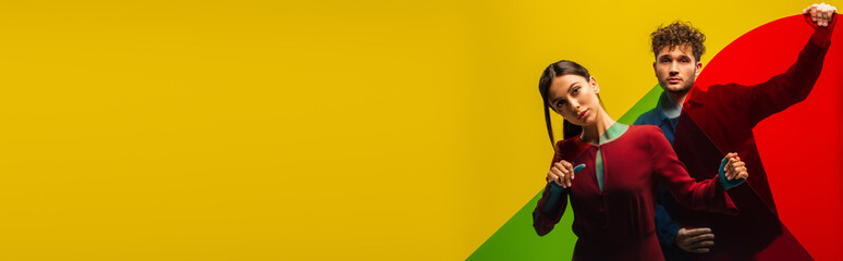 trendy man and fashionable woman holding different shapes glass while posing isolated on yellow, banner.