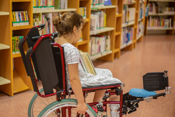  A schoolgirl in a wheelchair chooses books in the library.Life at the age of education of children...
