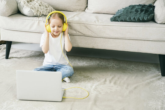 Little Girl 4 Years Old In Yellow Headphones In Front Of A Laptop.