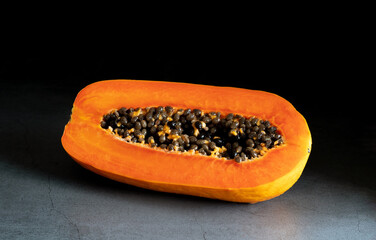 Half of a juicy orange papaya on a black background, macro. Copy space for your text.