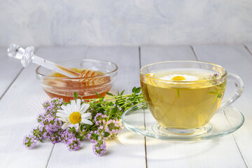 Herbal tea with chamomile and thyme in a transparent cup on a white wooden table