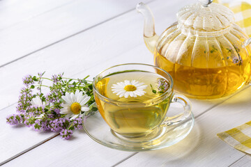 Herbal tea with chamomile and thyme in a transparent cup on a white wooden table