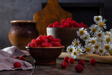 Fresh raspberries in a clay and wooden bowl on a dark wooden table