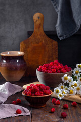 Fresh raspberries in a clay and wooden bowl on a dark wooden table