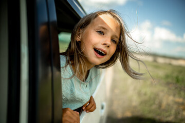 A five-year-old girl stuck her face out of the window of a moving car. Joyful emotions of a child