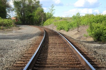 Railroad track with a green landscape view against a cloudy sky - Powered by Adobe