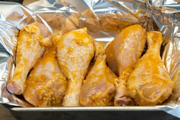 Closeup shot of marinated chicken drumsticks in an aluminum foil pan