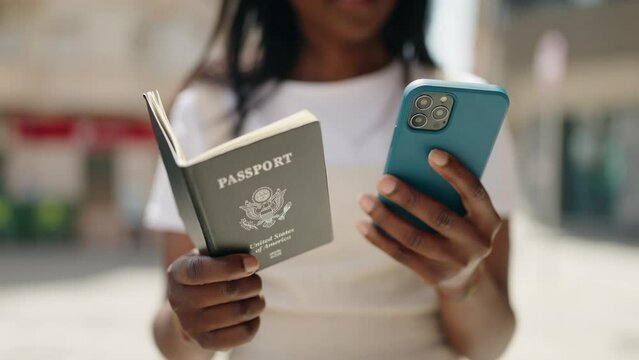 Young african american woman using smartphone holding united states passport at street