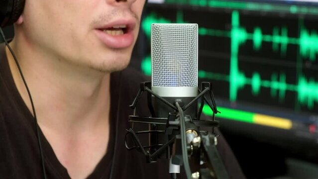 A close-up of a content creator's condenser microphone, a person who is streaming their podcast against an audio track on a monitor in the background. Male blogger recording voice over radio
