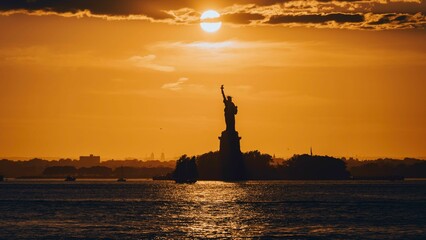 Silhouette shot of the Statue of Liberty on the coast of the ocean at sunset under an orange sky