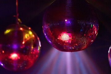 Closeup shot of disco balls hanging from the ceiling under bright pink and red lights in a club