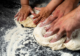 Adult and child preparing pizza dough close-up, dark table.