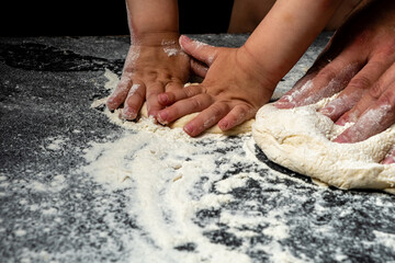 The hands of the kid and the father who prepare the pizza dough, dark background.