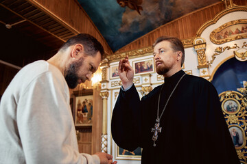 a priest blesses a bearded man in an Orthodox church after a festive church mass